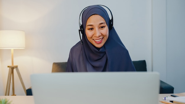 Muslim lady wear headphone watch webinar listen online course communicate by conference video call at night home office.