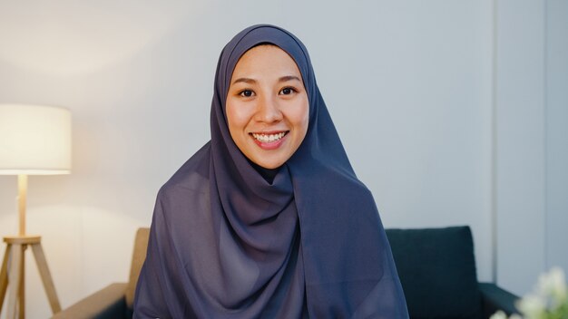 muslim lady wear hijab using computer laptop talk to colleague about plan in video call meeting while remotely work from home night at living room.