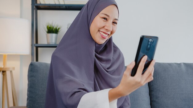 muslim lady wear hijab using phone video call talking with couple at home.