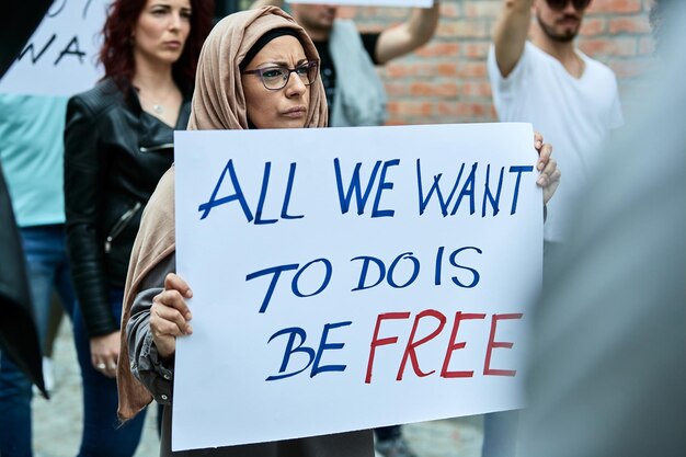 路上で人々の群衆と抗議しながら自由の碑文とプラカードを運ぶイスラム教徒の女性