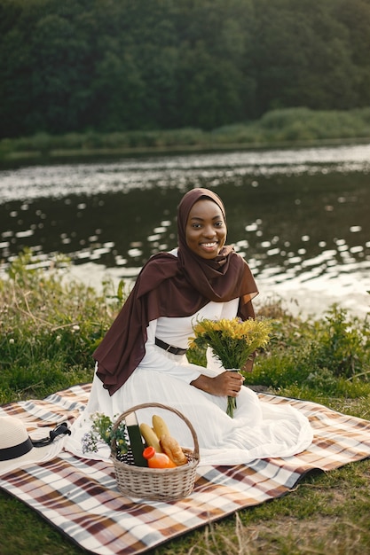 A muslim woman sits on the plaid picnic blanket near the river