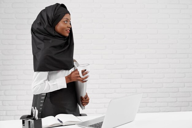 Muslim woman standing at workplace holding white folder