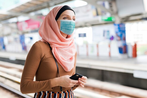 電車のプラットホームにマスクを持つイスラム教徒の女性