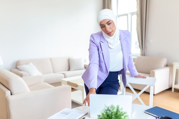 Мусульманка, работающая с компьютером дома Мусульманка, работающая с компьютером в комнате, пишущая бумагу Уверенность, симпатичная мусульманка Бизнес и финансы