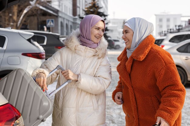 Muslim women with hijabs taking their luggage out of a car's trunk while being on vacation