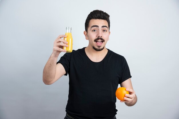 mustachioed man holding orange fruit with glass bottle of juice . 