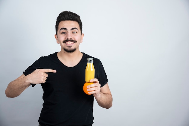 mustachioed man pointing at orange fruit with glass bottle of juice . 