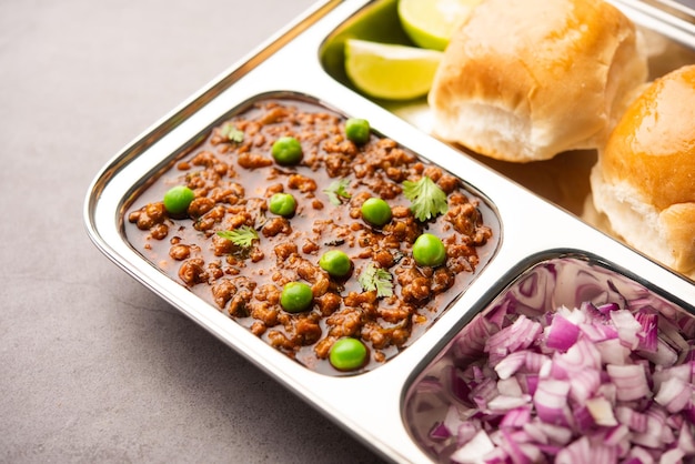 Mutton kheema pav or indian spicy minced meat served with bread or kulcha, garnished with green peas. moody background. selective focus