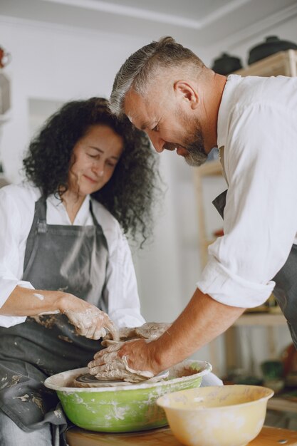 Mutual creative work. Adult elegant couple in casual clothes and aprons. People creating a bowl on a pottery wheel in a clay studio.