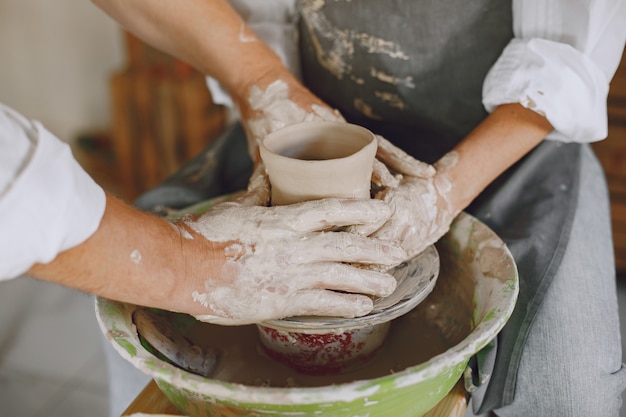 Mutual creative work. Adult elegant couple in casual clothes and aprons. People creating a bowl on a pottery wheel in a clay studio.