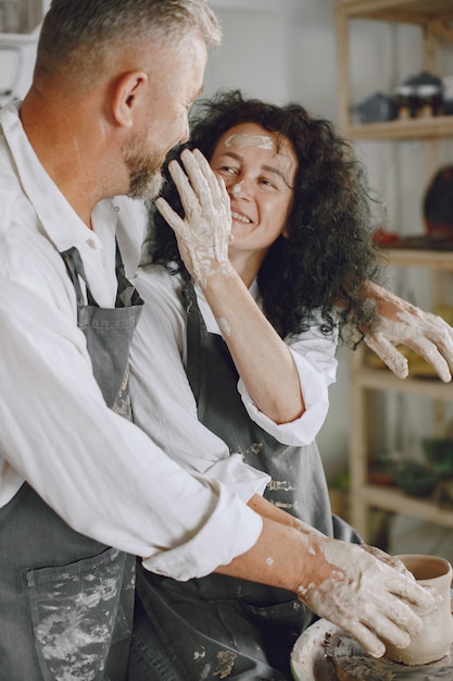 Mutual creative work. Adult elegant couple in casual clothes and aprons. People creating a bowl on a pottery wheel in a clay studio.