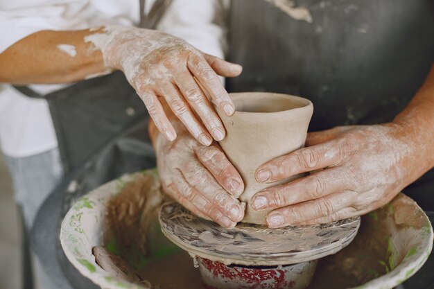 Mutual creative work. Adult elegant couple in casual clothes and aprons. People creating a bowl on a pottery wheel in a clay studio.