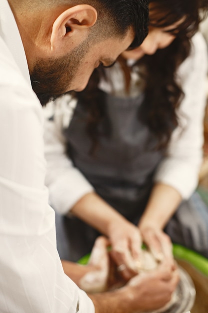 Mutual creative work. Elegant couple in casual clothes and aprons. People creating a bowl on a pottery wheel in a clay studio.