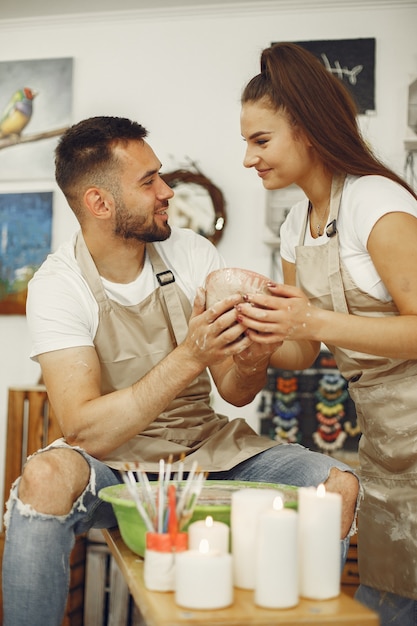 Mutual creative work. Young beautiful couple in casual clothes and aprons. People creating a bowl on a pottery wheel in a clay studio.