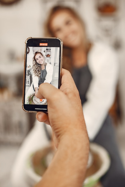 Foto gratuita lavoro creativo reciproco. giovane bella coppia in abiti casual e grembiuli. persone che creano una ciotola su un tornio in uno studio di argilla.