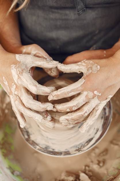 Mutual creative work. Young beautiful couple in casual clothes and aprons. People creating a bowl on a pottery wheel in a clay studio.