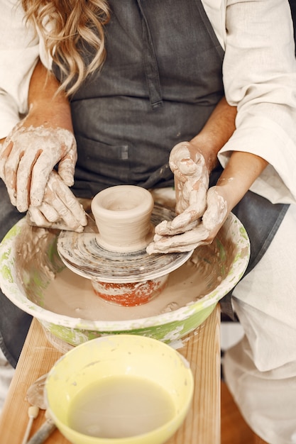 Foto gratuita lavoro creativo reciproco. giovane bella coppia in abiti casual e grembiuli. persone che creano una ciotola su un tornio in uno studio di argilla.