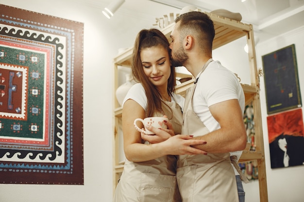 Free photo mutual creative work. young beautiful couple in casual clothes and aprons. people holds ceramic mug.