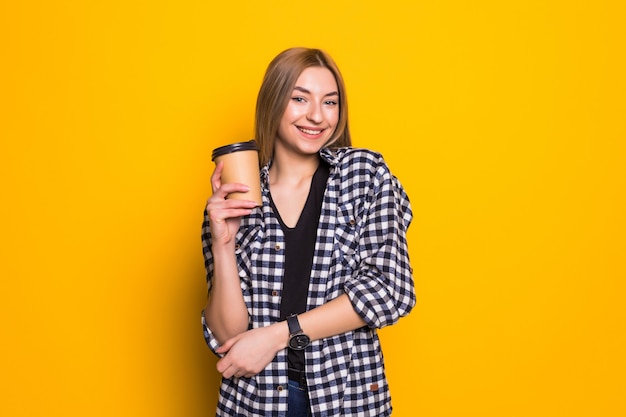 My best drink. Cute young woman in casual clothes with coffee mug in hands over yellow wall
