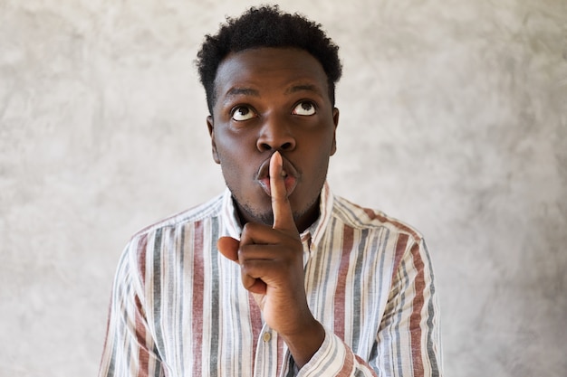 Mysterious young African male looking up, holding fore finger on his lips