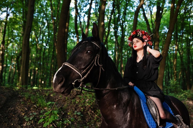 Мистическая девушка в венке в черном на лошади в лесу