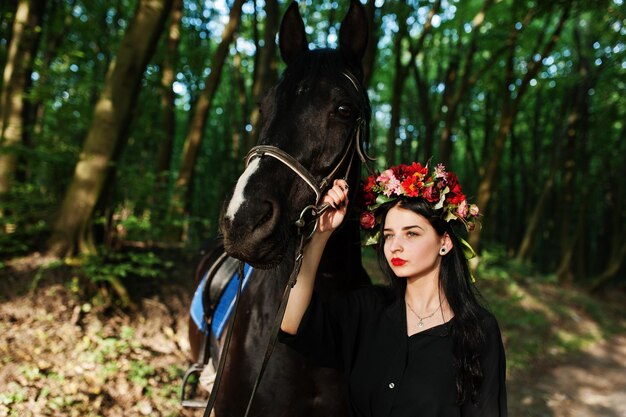 Mystical girl in wreath wear in black with horse in wood