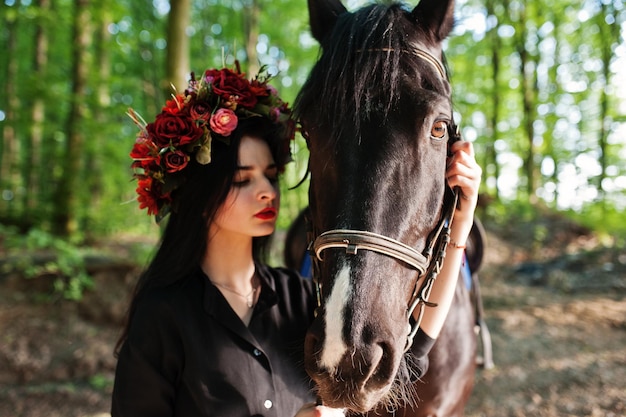 Мистическая девушка в венке в черном с лошадью в лесу
