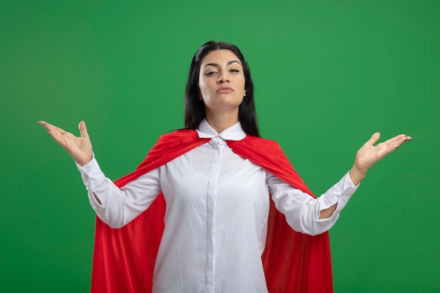 Free photo mystrerious young caucasian superhero girl showing empty hands with serious face isolated on green wall