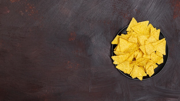 Nachos in black bowl on brown background