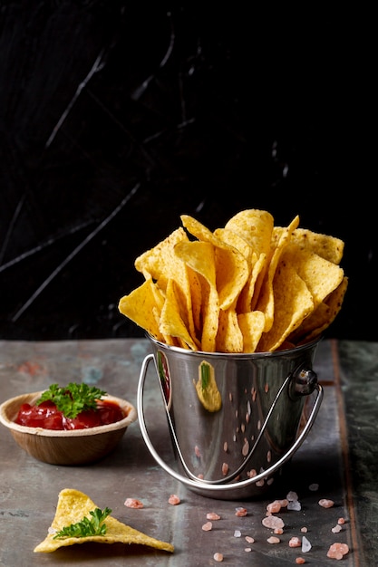 Nachos in bucket and tomato sauce in bowl with parsley