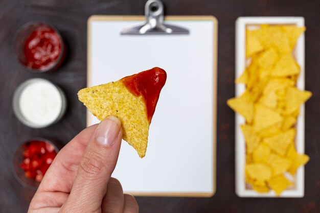 Nachos in ketchup in hands above table with vegetables 