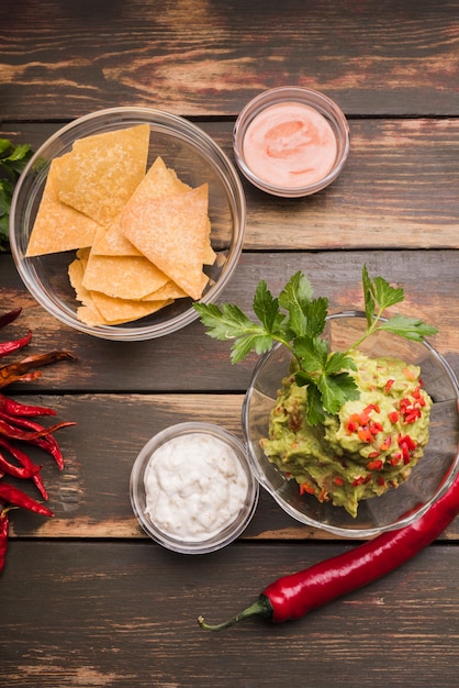 Nachos near guacamole and sauce in bowls among chili