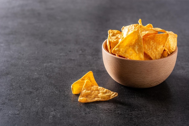 Nachos in wooden bowl on black slate background