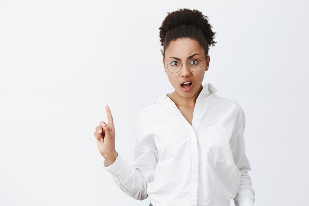 Nah, no way. Portrait of feminine displeased and pissed attractive emotive dark-skinned woman with curly hair, gesturing with finger in no or refusal gesture, standing over gray wall