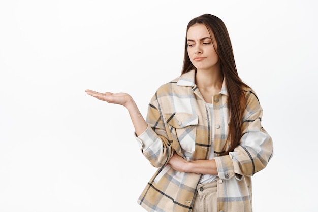 Free photo nah that is bad displeased and skeptical young woman frowning grimacing while looking at her empty open hand holding something awful or unpleasant standing over white background