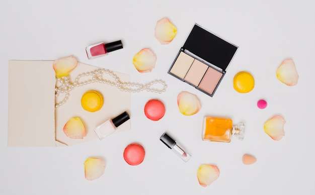 Free photo nail varnish bottle; rose petals; necklace; lipstick; macaroons and perfume bottle isolated on white background