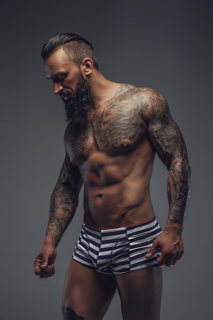 Free photo naked bearded man with tattooed body standing on a grey background.