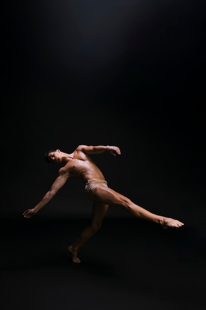 Naked graceful man dancing against black background