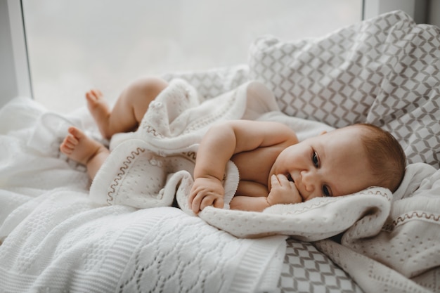 Голый новорожденный мальчик лежит на мягком одеяле перед ярким окном