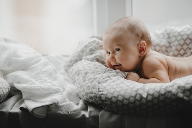 Голый новорожденный мальчик лежит на мягком одеяле перед ярким окном
