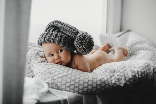 Free photo naked newborn boy in a warm winter hat lies on the soft blanket before a bright window