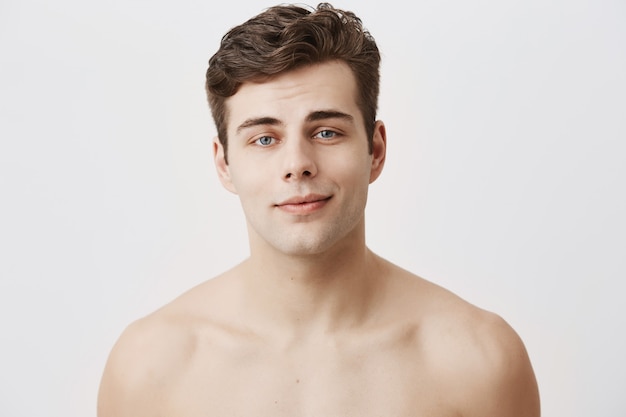 Naked positive caucasian male with pure healthy skin and dark hair, appealing blue yes, smiles gently as being glad after date with grifriend. Beauty and youth concept.