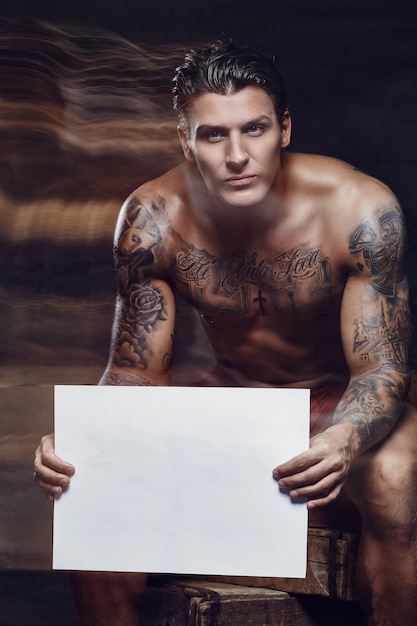 Free photo naked tattooed muscular man posing in studio. your text here.