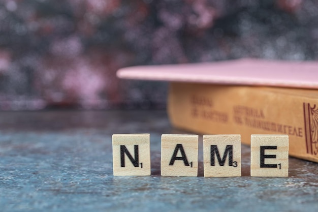 Free photo name writing with black letters on wooden dices with an old book around. high quality photo