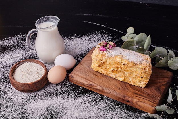 나폴레옹 케이크는 계란, 우유, 밀가루 그릇 블랙 테이블에 말린 꽃 씨앗으로 장식.