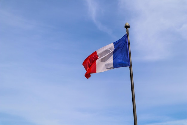 The national flag of france on the flagpole develops in the wind against the blue sky