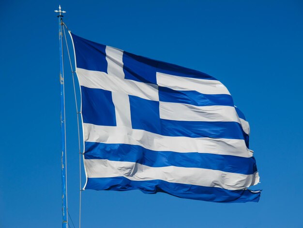 The national flag of greece on the flagpole develops in the wind against the blue sky