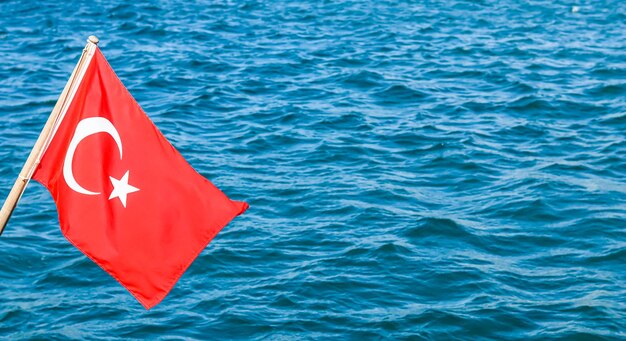 National flag of turkey on a flagpole in the wind against a background of blue sea.