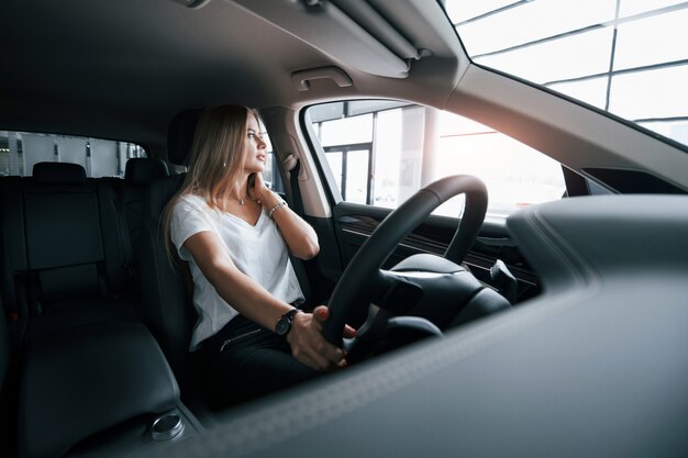 自然な日光。サロンで現代の車の女の子。昼間の屋内。新しい車を買う