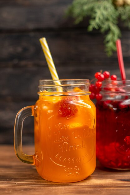 Natural fresh juices in bottles served with tubes and fruits on a brown wooden background